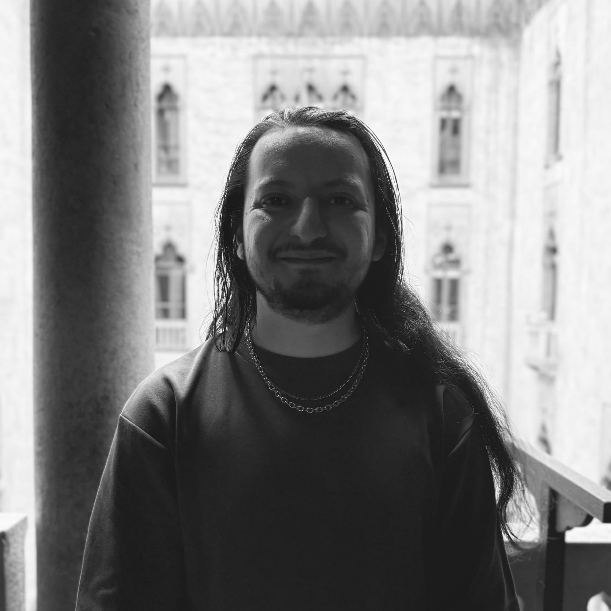 What my mother would describe as a handsome man standing next to a pillar with an older brick building behind him. The image is in gray scale and located in the Isabella Gardner Museum.